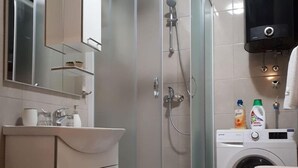 A modern bathroom with a glass-enclosed shower, a washing machine, and a toilet. - Apartments Šišević (Dubrovacko Primorje)