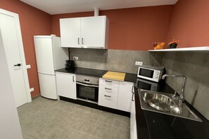 A compact kitchen with white cabinets, a microwave, a sink, and a small refrigerator.