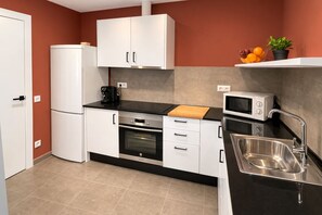 A compact kitchen with white cabinets, a black countertop, a stainless steel sink, and a microwave.