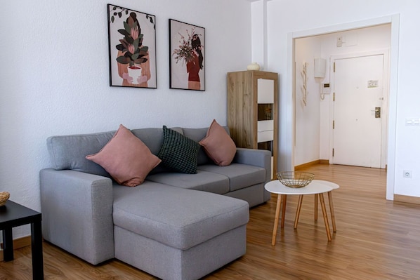 A modern living room with a grey sectional sofa, a small round table, and two framed artworks on the wall.
