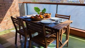A wooden table with chairs, a bowl of fruit, and a basket of pastries on a balcony with a view.