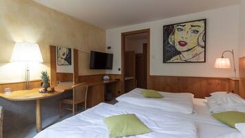 A hotel room with two beds, a desk with a lamp, a television, and artwork on the walls.
