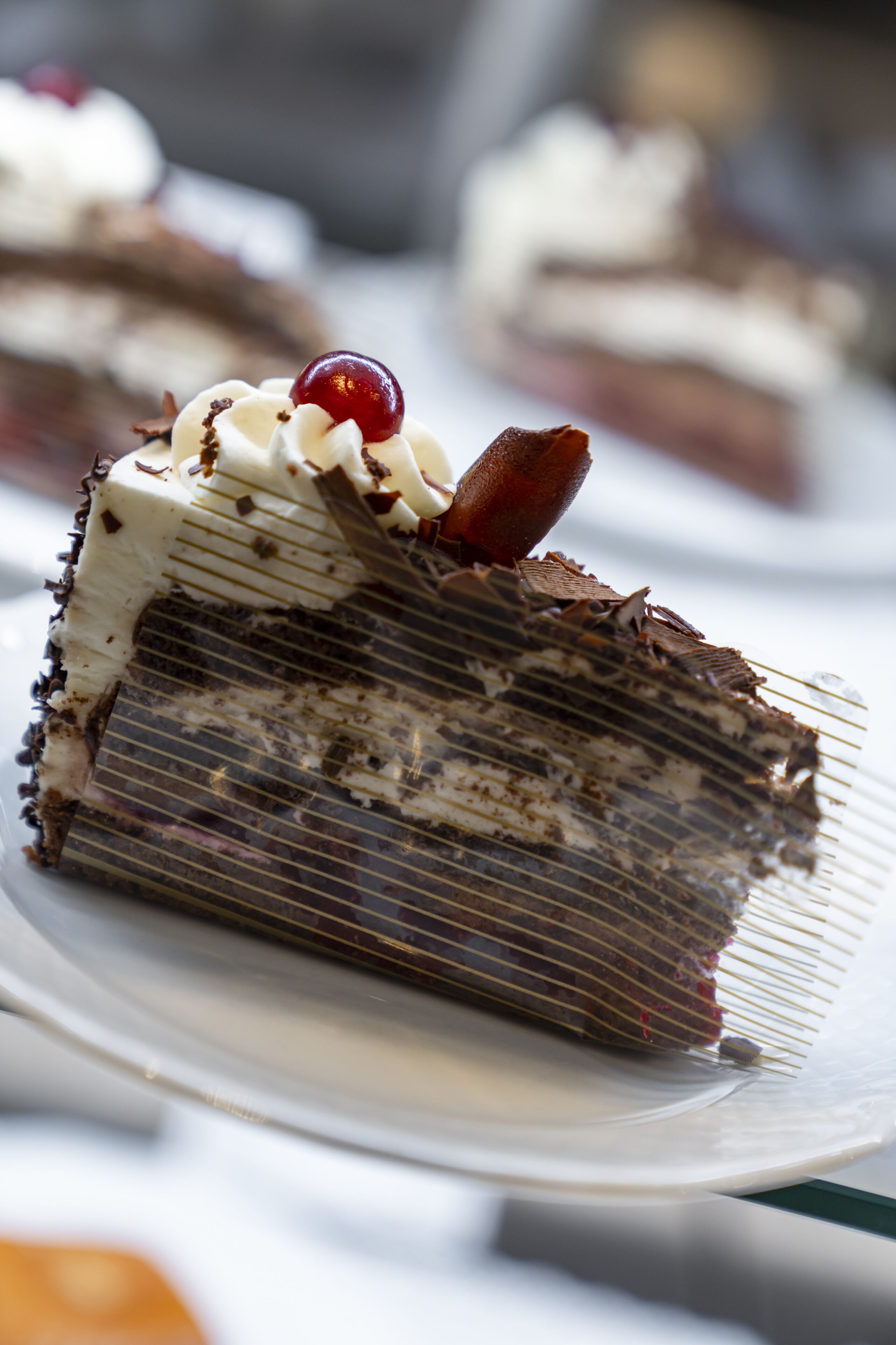 A slice of chocolate cake with whipped cream and a cherry on top, served on a white plate.
