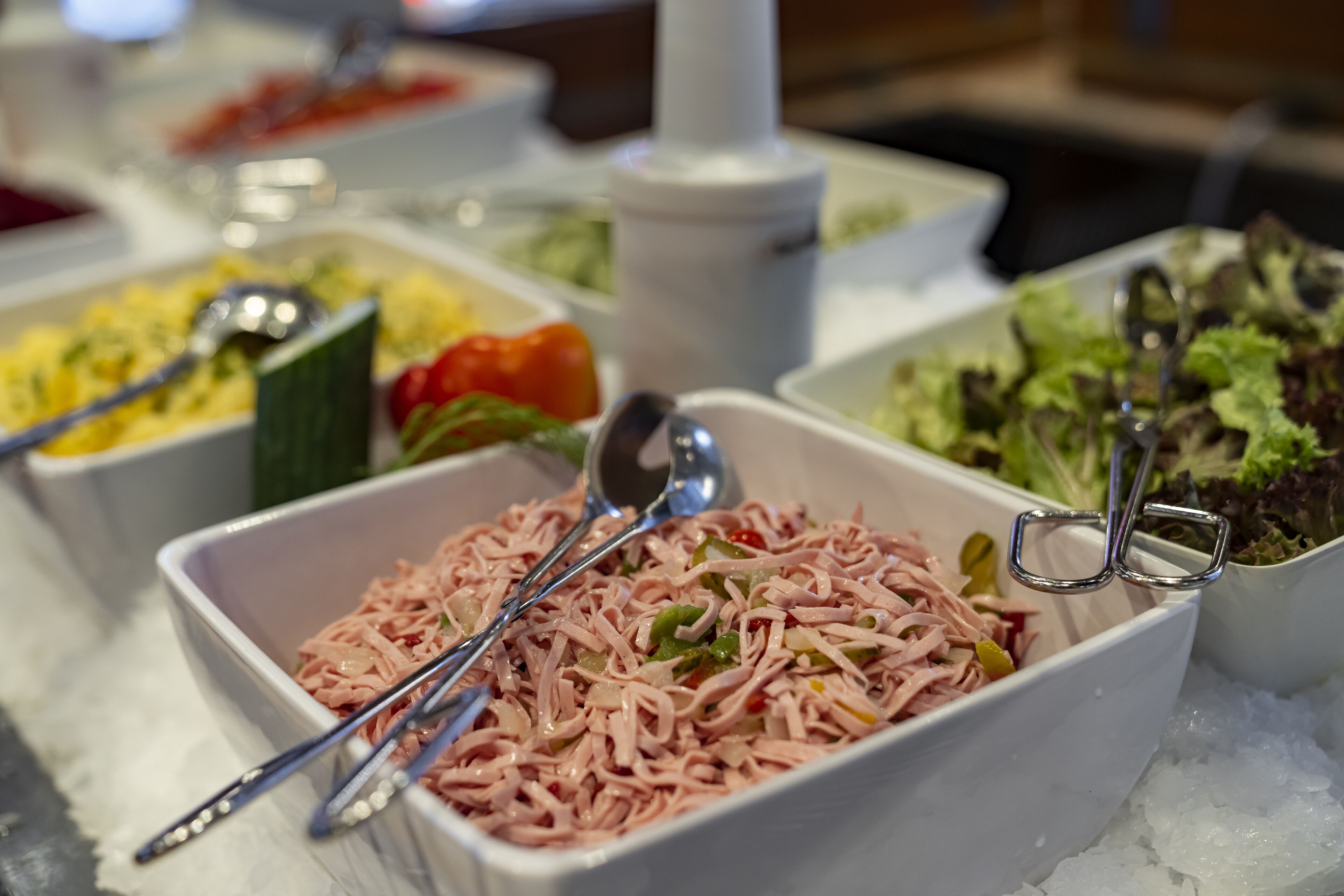 Un bufé con diversos platos, incluyendo una ensalada, un guiso de carne deshebrada y un plato de verduras.