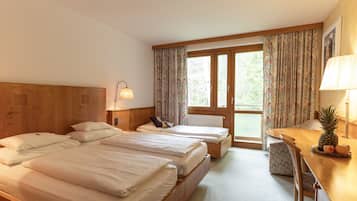 Habitación de hotel con dos camas, un escritorio de madera con lámpara, una silla y vistas al exterior a través de un ventanal grande.