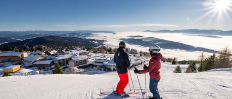 A ski resort with snow-covered slopes, a clear sky, and a view of a town in the background.