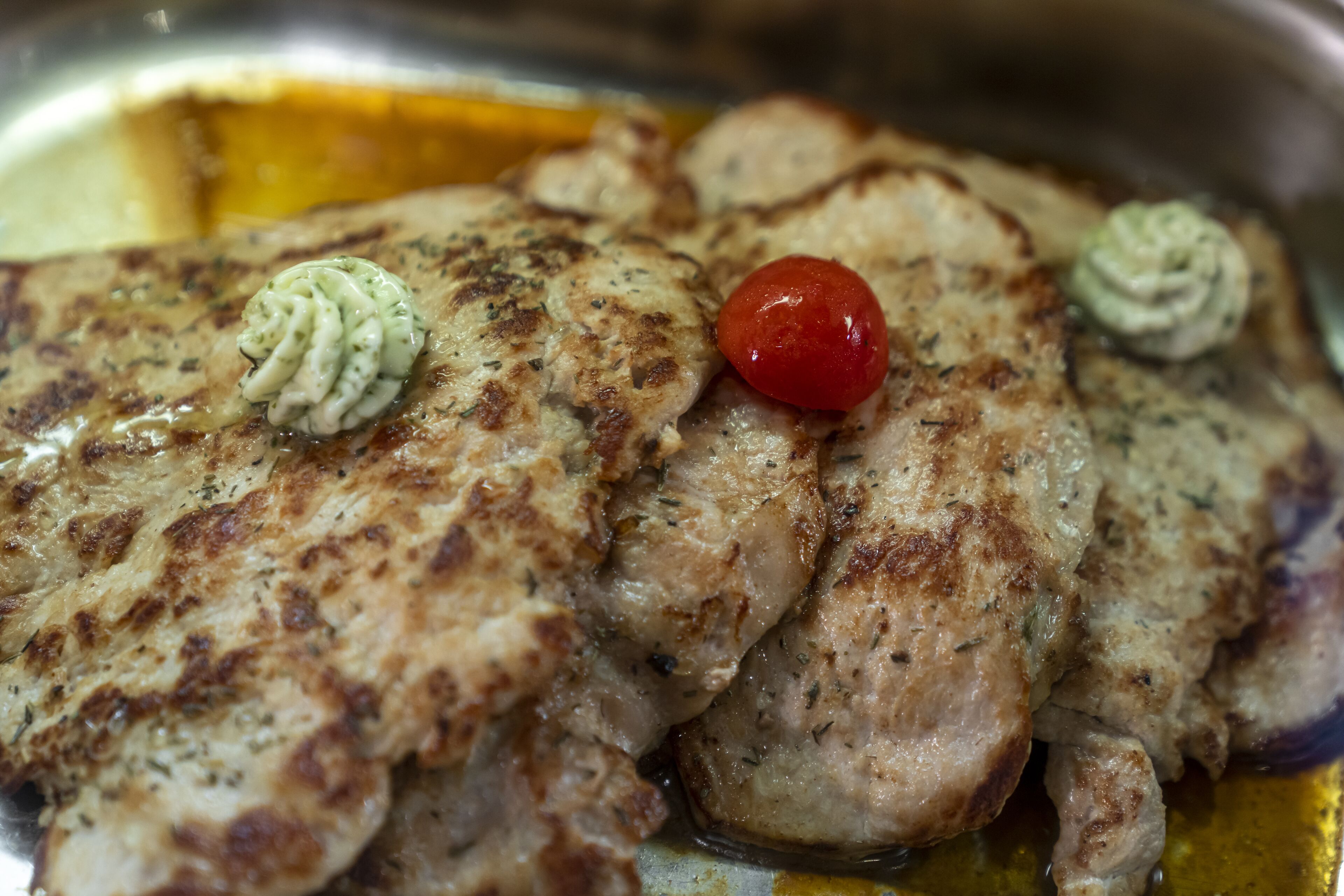Gegrillte Hähnchenbrust mit Kräutern und einer Kirschtomate auf einem Teller.