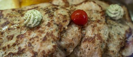 Grilled chicken breasts with herbs and a cherry tomato on a plate.