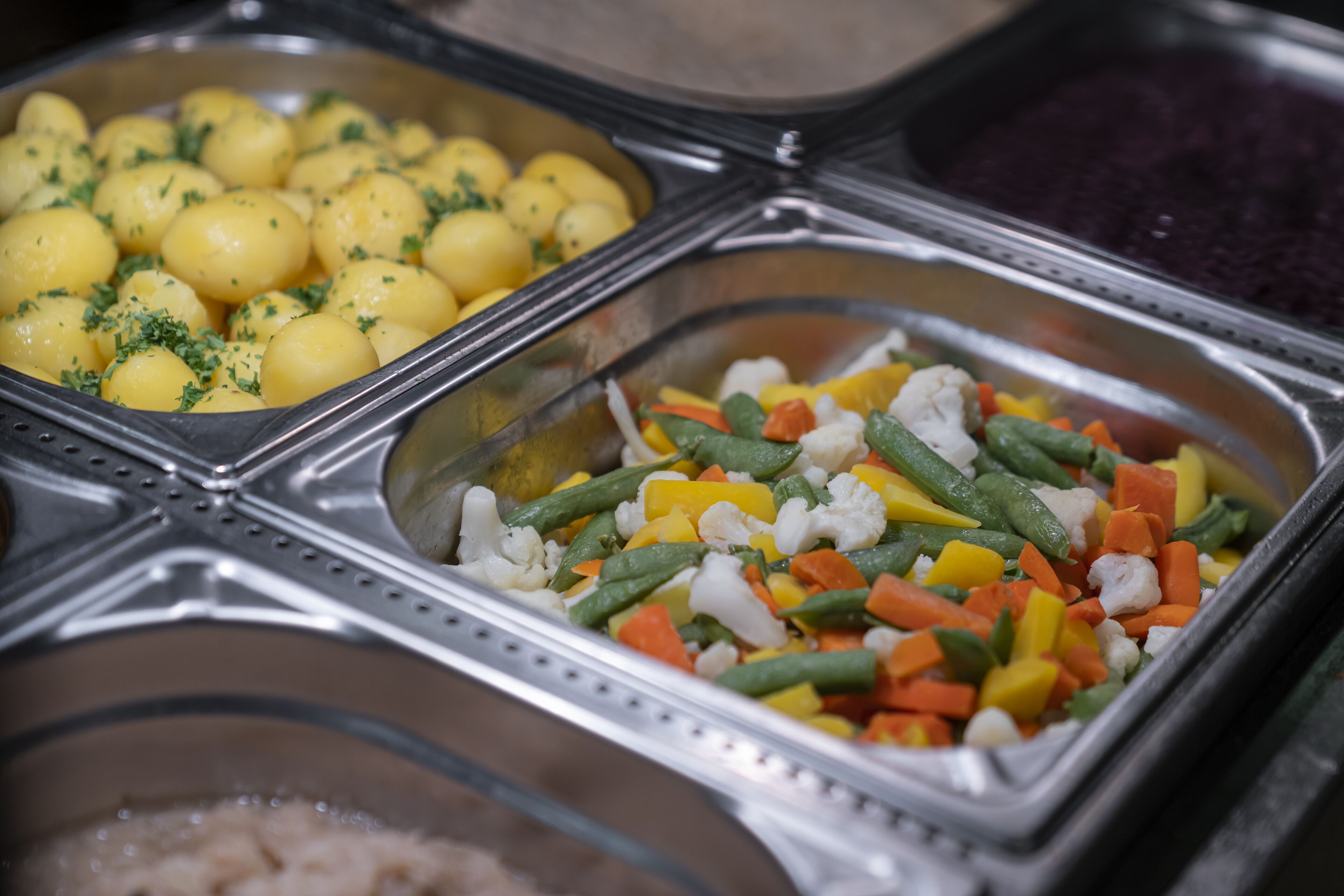 Un buffet proposant une variété de plats, notamment des pommes de terre, des haricots verts, des carottes et du chou-fleur.