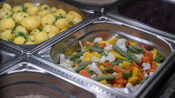 Un buffet proposant une variété de plats, notamment des pommes de terre, des haricots verts, des carottes et du chou-fleur.