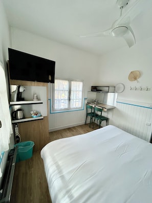 A compact hotel room with a bed, a desk, a chair, a TV, a window, and a ceiling fan. - Hotel Oasis (Argelès-sur-Mer)