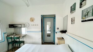 A hotel room with a bed, a desk with a chair, a kitchenette, and a bathroom visible through an open door. - Hotel Oasis (Argelès-sur-Mer)