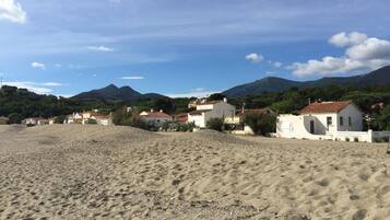 A beach with white buildings, a sandy foreground, and mountains in the background.