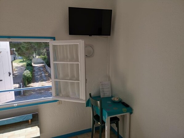 Una habitación con ventana, una mesita con mantel color turquesa y un televisor montado.