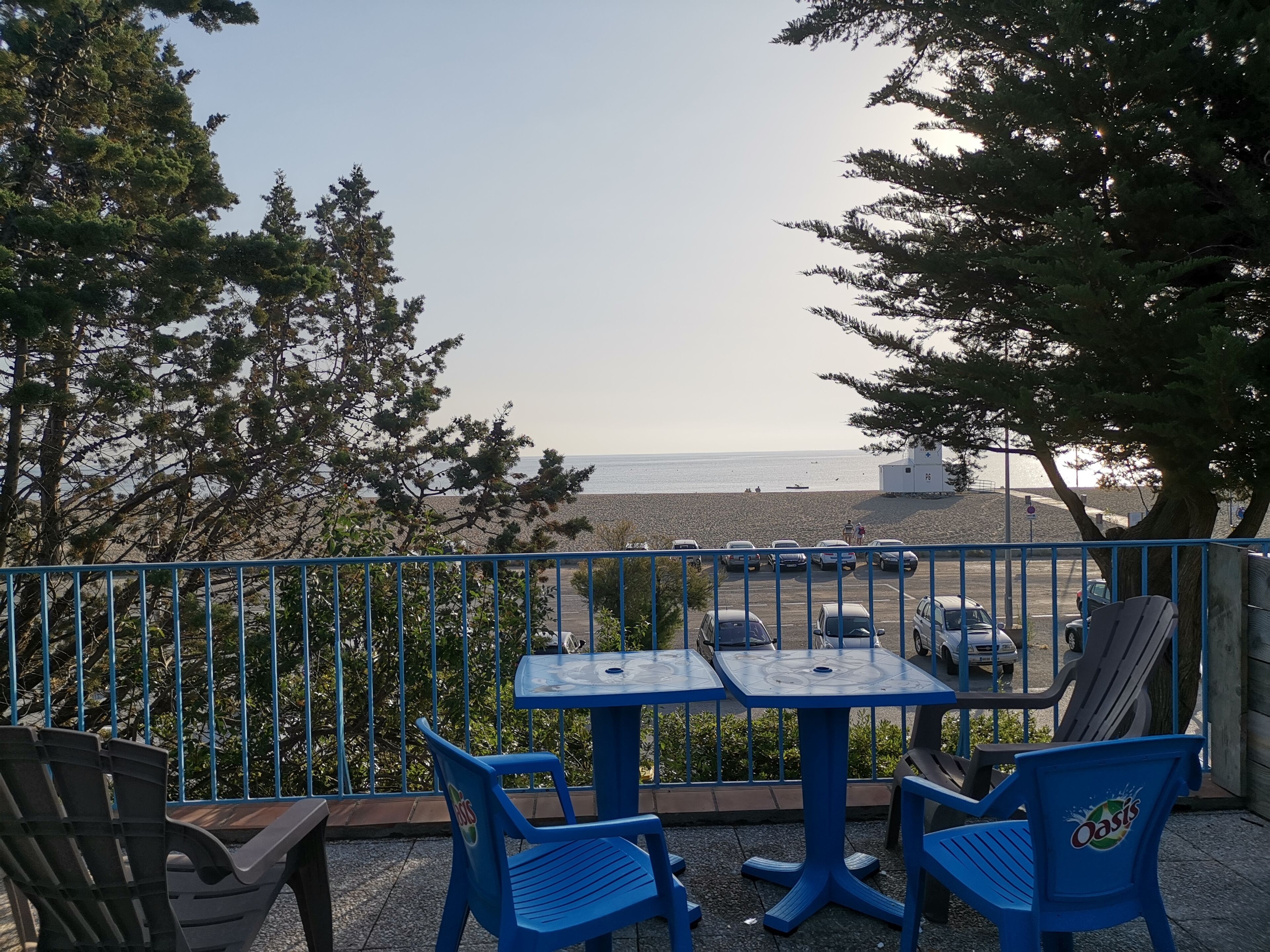 En terrasse med blå stole og borde, der ligger ud til en strand.
