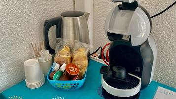 A coffee maker, a kettle, a basket of bread, and a cup on a teal table.
