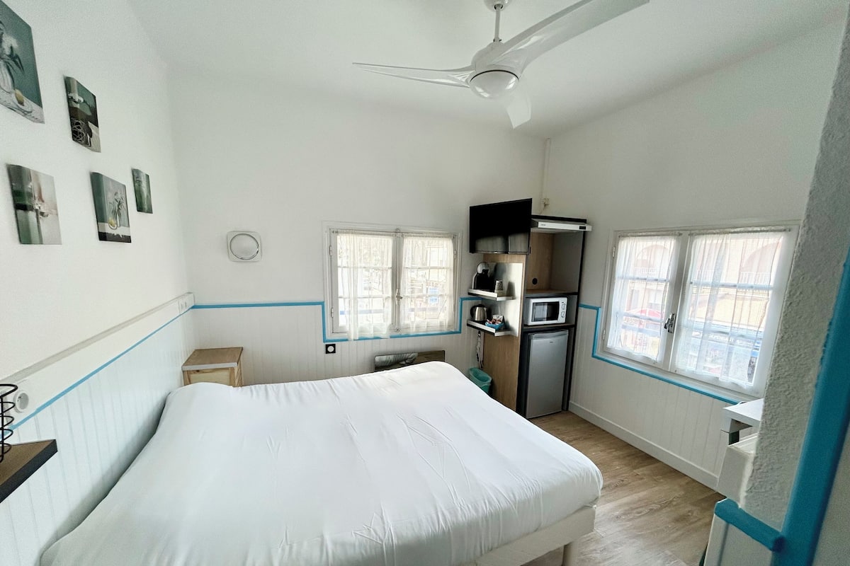 A bedroom with a bed, a ceiling fan, a microwave, and a small refrigerator.