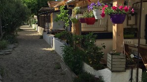 A narrow alleyway with a building on the right featuring a covered porch with hanging flower baskets and potted plants. - Hotel Oasis (Argelès-sur-Mer)