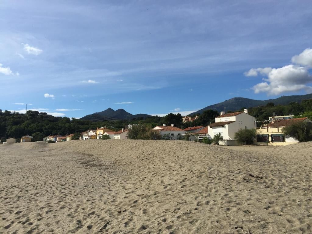 A sandy beach with houses in the background and mountains in the distance.
