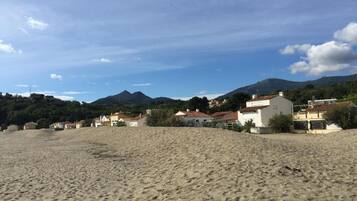 A sandy beach with houses in the background and mountains in the distance.