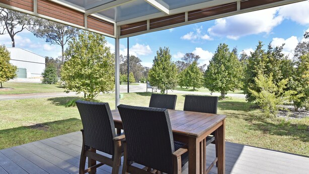 Un patio exterior con una mesa y cuatro sillas, rodeado por un área techada que ofrece vistas a un césped y árboles.