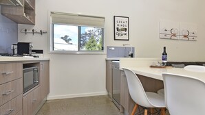 Una cocina moderna con armarios de madera, horno empotrado, lavavajillas y ventana con vistas a árboles.