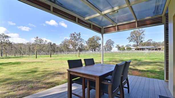 An outdoor patio with a table and chairs, overlooking a grassy field and trees.