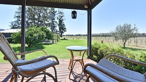 A covered outdoor seating area with wicker furniture, a small table, and a view of a vineyard.