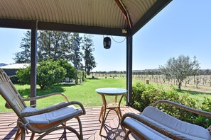 A covered outdoor seating area with wicker furniture, a small table, and a view of a vineyard.