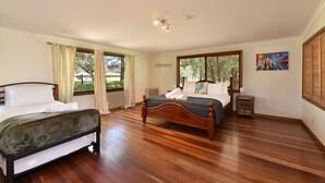 A bedroom with two beds, a wooden floor, a ceiling fan, and large windows with curtains.