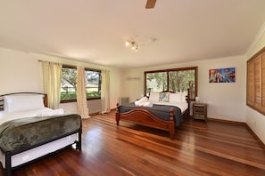 A bedroom with two beds, a wooden floor, a ceiling fan, and large windows with curtains.