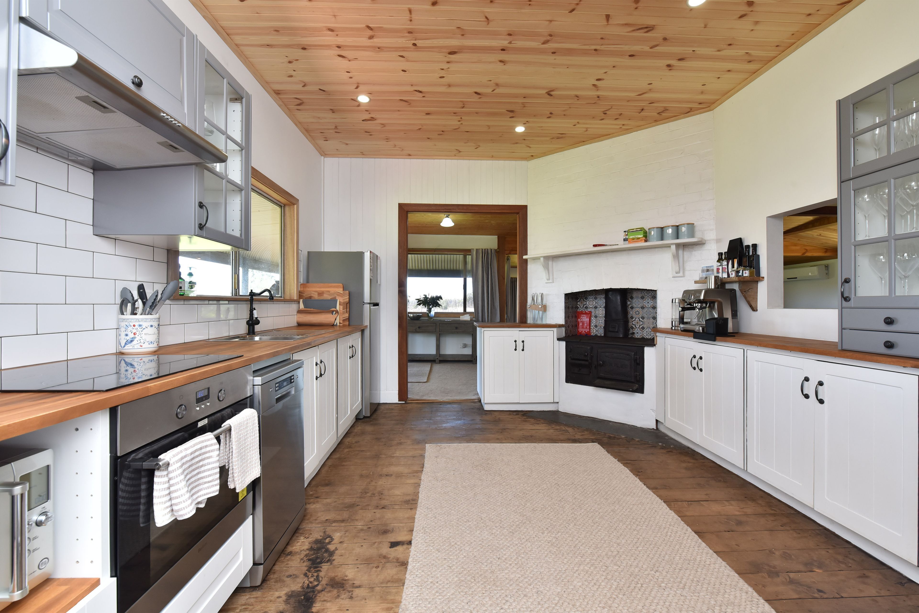 A modern kitchen with white cabinetry, stainless steel appliances, and a wooden ceiling.