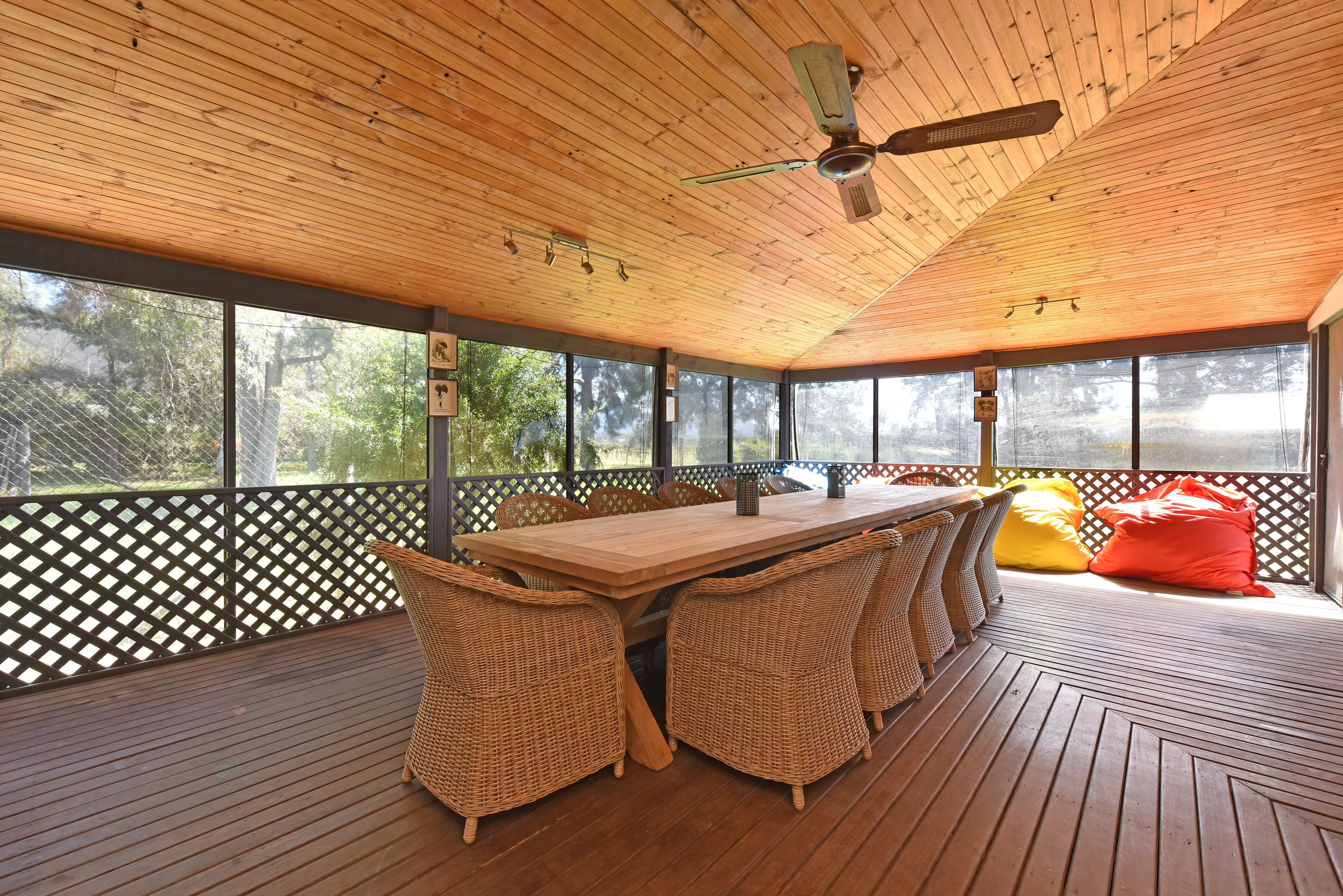 A covered outdoor area with a wooden table and wicker chairs, surrounded by a wooden deck and a lattice fence.