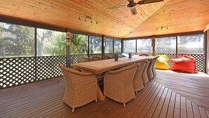 A covered outdoor area with a wooden table and wicker chairs, surrounded by a wooden deck and a lattice fence.