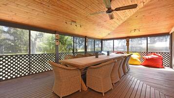A covered outdoor area with a wooden table and wicker chairs, surrounded by a wooden deck and a lattice fence.