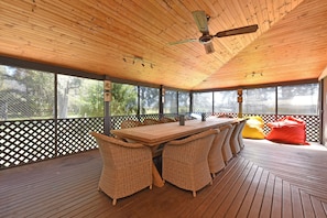 A covered outdoor area with a wooden table and wicker chairs, surrounded by a wooden deck and a lattice fence.