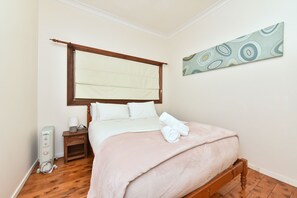 Een slaapkamer met een houten bed, een nachtkastje met een lamp en een kunstwerk aan de muur.
