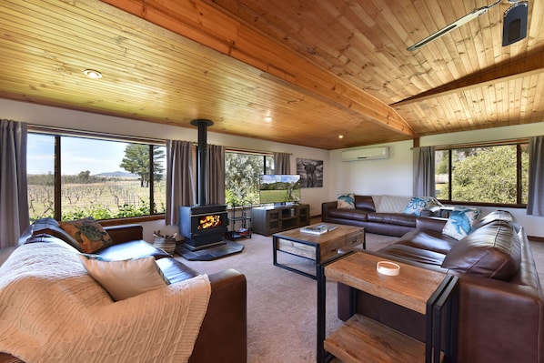 A cozy living room with a fireplace, leather sofas, and large windows offering a view of the outdoors.