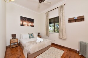 A bedroom with a bed, nightstands, a window with curtains, a radiator, and a wall-mounted shelf.