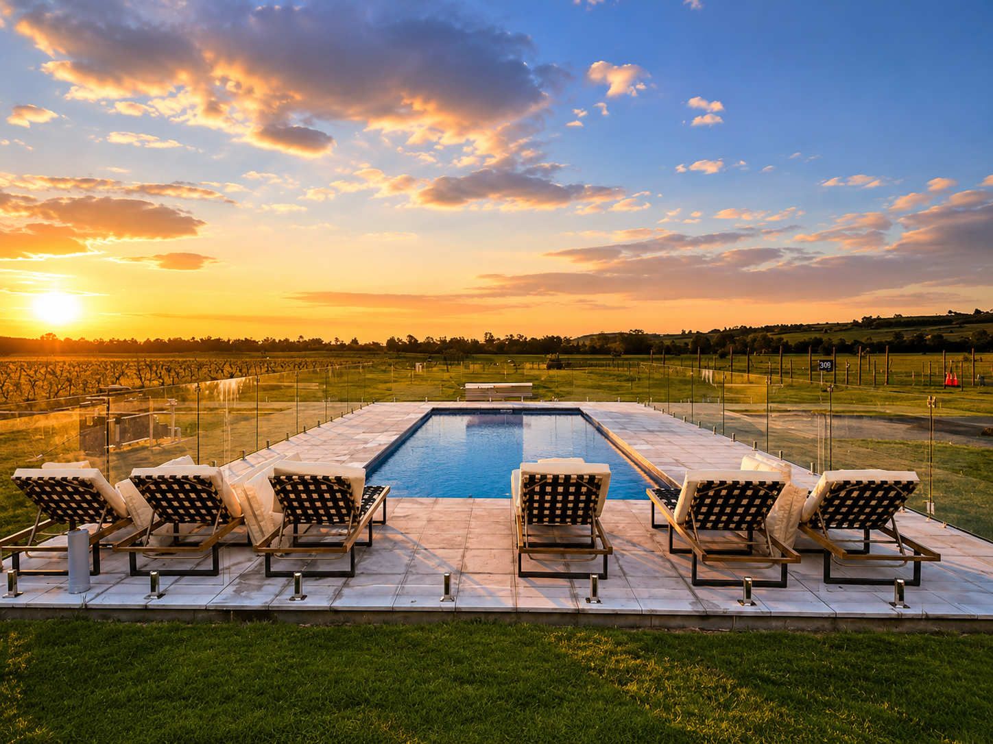 A swimming pool with lounge chairs and a view of a vineyard at sunset.