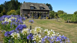 Uma casa rústica com varanda, rodeada por um jardim com flores azuis e brancas.