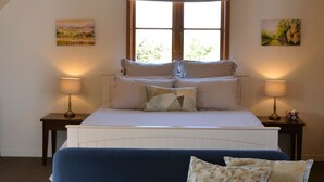 Quarto com uma cama, duas mesas de cabeceira com luminárias, um sofá azul e duas pinturas nas paredes.