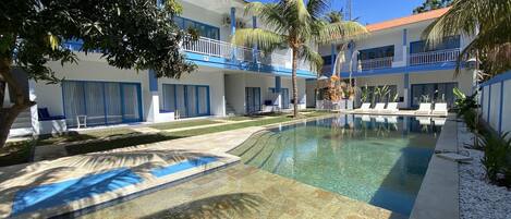 Un hôtel doté d’une piscine, de palmiers et surplombant un ciel bleu azur.