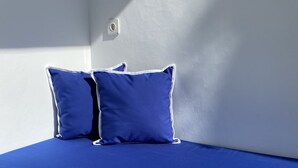 A bed with a blue mattress and pillows, positioned against a white wall with a light switch. - Kura Kura Divers Lodge (Karangasem)