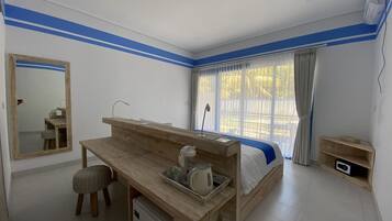 A bedroom with a wooden desk, a small stool, a bed with a blue blanket, and a window with curtains.