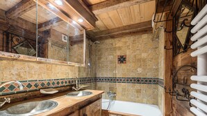 Une salle de bain rustique avec des meubles en bois, un double lavabo, une baignoire et une zone de douche carrelée.