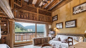 Une pièce chaleureuse avec un plafond en bois, une grande fenêtre donnant sur les montagnes, un canapé, une table ronde en bois et un tapis à motifs.
