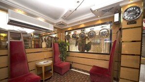 A hotel lobby with red velvet chairs, a small round table, and a wall displaying clocks from various cities. - Downtown Hotel (Dubai)
