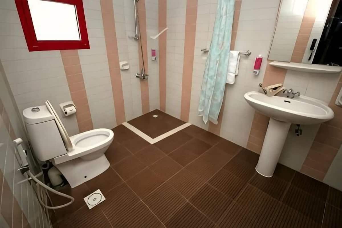 A bathroom with a toilet, shower, sink, and a mirror.