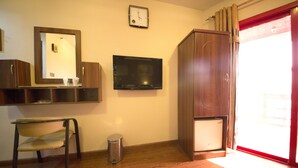 A room with a wooden floor, a television mounted on the wall, a wooden cabinet, a small trash bin, and a chair. - Downtown Hotel (Dubai)